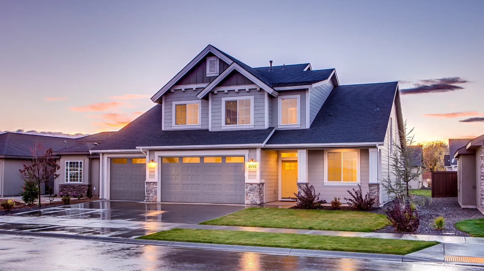 Dusk view of a gray two-story home under a dark shingle roof